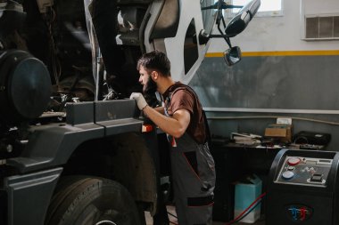 Tamirci, garajın içindeki bir kamyon motoru üzerinde özenle çalışıyor. Ağır vasıflı araçların bakımını ve tamirini yapıyor.