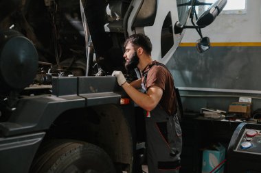 Bir atölyede usta bir oto tamircisi büyük bir kamyon motorunu özenle tamir ediyor, uzmanlık gösteriyor ve otomotiv bakımına odaklanıyor