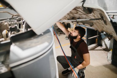 Araç bakım ve onarımı için araç ve uzmanlık kullanan otomobil tamircisi bir garajda kamyon motorunu kontrol ediyor