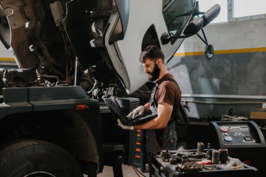 Otomobil tamircisi garajdaki bir kamyon arızasını teşhis etmek için dizüstü bilgisayar kullanıyor, bakım ve onarım yapıyor.