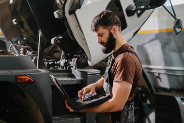 Otomobil tamircisi garajdaki bir kamyon arızasını teşhis etmek için dizüstü bilgisayar kullanıyor, bakım ve onarım yapıyor.