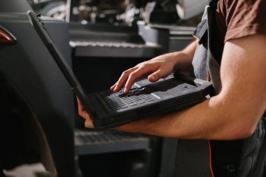 Modern bir araç tamir atölyesinde dizüstü bilgisayar kullanan tamirci, performansı optimize ediyor ve yol değerliliğini sağlıyor