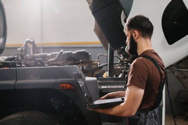 Otomobil tamircisi, bir garajda kamyon motoru sorunu teşhis etmek için dizüstü bilgisayar kullanıyor, bakım ve onarım yapıyor.