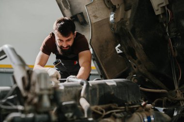 Otomobil tamircisi garajdaki bir kamyon motoru üzerinde özenle çalışıyor, gerekli bakım ve onarım işlerini titizlikle yapıyor.