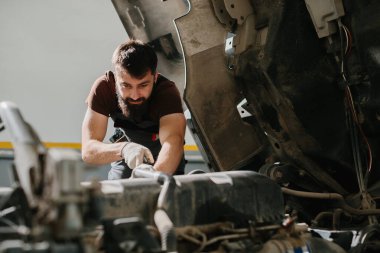 Odaklanmış bir tamirci garajda bir kamyon motoru üzerinde çalışıyor. Uzmanlık ve araç bakım ve onarımına olan bağlılığını gösteriyor.