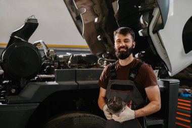 Otomobil tamircisi garajda büyük bir kamyon motorunu ustalıkla tamir ediyor, teknik beceriler ve araç bakımına adanmışlık sergiliyor