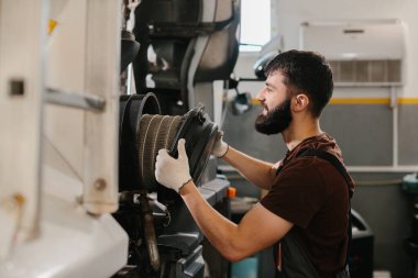 Oto tamircisi eldiven ve tulum giyer, yoğun bir tamirhanede bir kamyonun hava filtresini değiştirir, en iyi motor performansını sağlar.