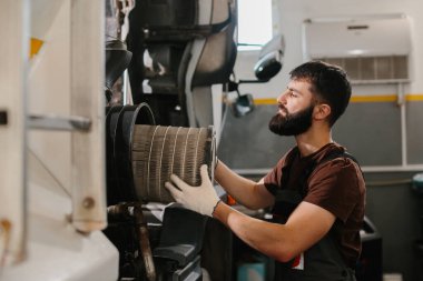 Tamirci eldiven takıyor. Yoğun bir tamirhanede kirli hava filtresi değiştiriyor. Maksimum motor performansı ve bakım sağlıyor.
