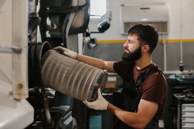 Oto tamircisi, yoğun bir tamirhanede çalışırken bir kamyonda kirli hava filtresini değiştiriyor ve en iyi motor performansını sağlıyor.