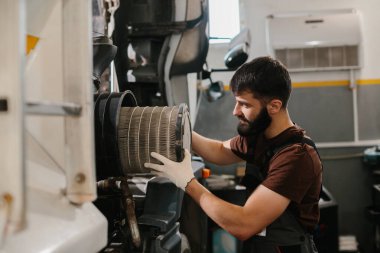 Eldiven giyen oto tamircisi, yoğun bir tamirhanenin içindeki kirli hava filtresini değiştiriyor ve maksimum motor performansını sağlıyor.