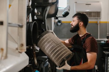 Oto tamircisi, yoğun bir tamirhanedeki bir kamyonun bakımını yaparken kirli hava filtresi tutuyor ve en uygun araç performansını sağlıyor.