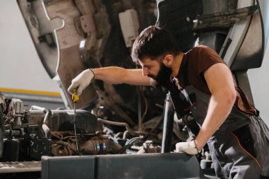 Tamirci tulum giyer ve eldiven giyer tamirhanenin bakım servisi sırasında bir kamyon motorunun yağ seviyesini kontrol eder.