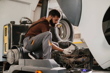 Profesyonel bir tamirci, bir tamirhanedeki bakım sırasında büyük bir kamyon motorunda yağ seviyesini kontrol ediyor.