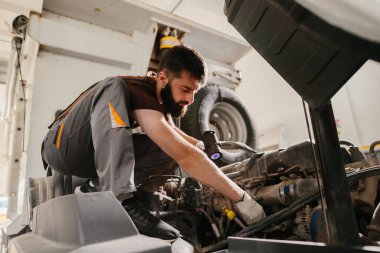 Garajda kamyon motorunu incelerken el feneri kullanan profesyonel bir tamirci.