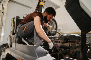 Tamirci, profesyonel bir garajda planlanan bakım kontrolü sırasında bir kamyon motorunun yağ seviyesini kontrol ediyor.
