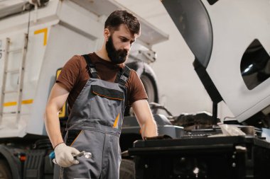 Otomobil tamircisi ingiliz anahtarı, bir garaj atölyesinde kamyon motoru üzerinde çalışıyor, bakım veya onarım işi yapıyor.