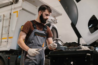 Profesyonel oto tamircisi garajın içinde bir kamyon motoru üzerinde çalışıyor, bakım ve onarım yapıyor.