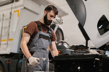 Garaj atölyesinde bir kamyon motoru üzerinde çalışan profesyonel bir tamirci, bir ingiliz anahtarı tutuyor ve bakım ve onarım işlerini yapıyor.