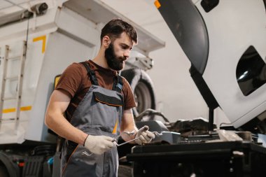 Oto tamircisi eldiven takıyor ve iyi donanımlı bir garajda araç tamirine adanmış bir kamyoneti incelemeye odaklanıyor.