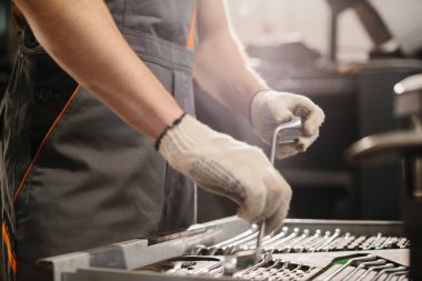 Tamirci eldiven giyip araç atölyesindeki alet çantasından doğru anahtarı seçiyor ve kamyon bakımına hazırlanıyor.