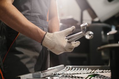 Tamirci eldiven takıyor ve özenle çalışıyor. Yoğun bir kamyon tamirhanesinde organize bir alet kutusundan anahtar seçiyor.