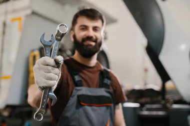 Gülümseyen tamirci, meşgul bir kamyon tamirhanesinde iki anahtarı gururla tutuyor. Otomotiv bakımı ve servis alanında uzmanlık gösteriyor.
