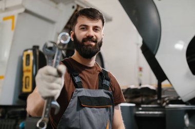 Meşgul bir tamirhanede çalışırken anahtarı elinde tutan kendine güvenen tamirci, otomotiv bakımı alanında beceri ve uzmanlık gösteriyor.
