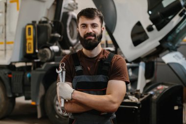 Bir atölyede deneyimli bir tamirci elinde aletlerle büyük bir kamyonu tamir ediyor. Profesyonel ekipmanlarla endüstriyel ortam