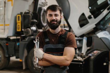 Anahtarları tutan kendinden emin bir tamircinin portresi, bir kamyon tamirhanesinde gülümseyen, otomotiv endüstrisinde uzmanlık ve profesyonellik sergileyen