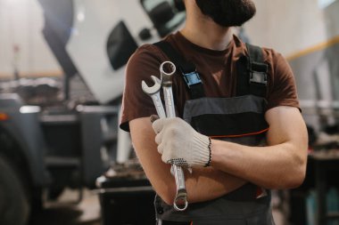 Profesyonel tamirci garajda kamyonları tamir ederken anahtarlarını tutuyor. Uzmanlık ve araç bakımına olan bağlılığını gösteriyor.