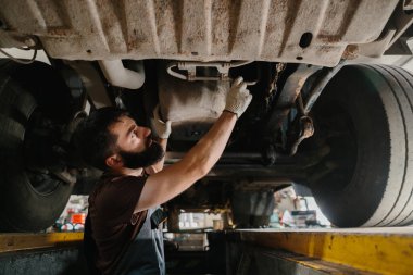 Tamirci, bir garajda büyük bir kamyonun altını özenle onarıyor. Otomotiv bakımında uzmanlık ve dikkat gösteriyor.