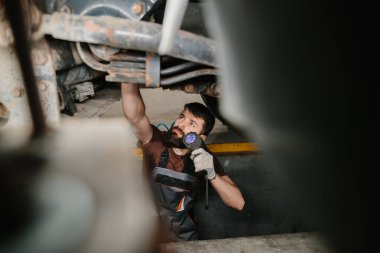 Tamirhanedeki bir kamyonun şasisini incelerken el feneri kullanan oto tamircisi.