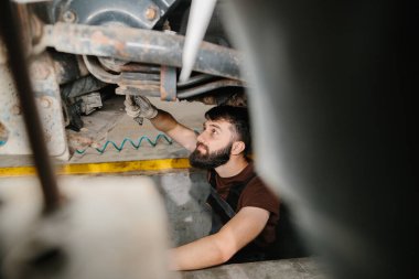 Bir kamyonun altında çalışan genç bir tamirci profesyonel bir garajda tamir ve onarım için ingiliz anahtarı kullanıyor.