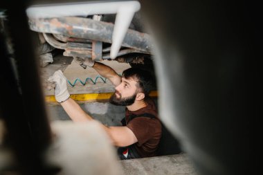 Bir kamyonun altında çalışan yetenekli bir tamirci, profesyonel bir garaj ortamında bakım ve onarım yapıyor.