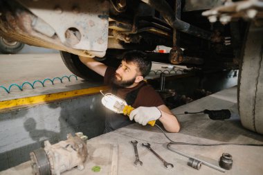 Tamirhanedeki bir kamyonun şasisini incelerken iş lambasını kullanan oto tamircisi.