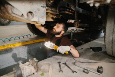Tamircide bir kamyonun şasisini incelerken iş lambası kullanan oto tamircisi.