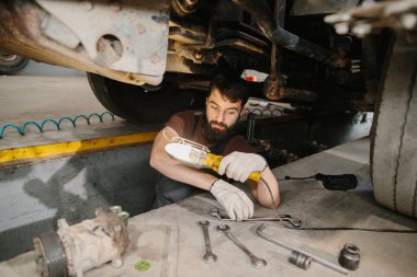 Tamir atölyesindeki bir kamyonu kontrol eden tamirci, aracın bakımını ve teşhisini yapmak için çalışma lambasını kullanarak aracı aydınlatıyor.