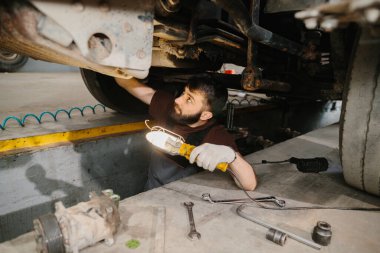 Tamircide bir kamyonun şasisini incelerken iş lambası kullanan oto tamircisi.