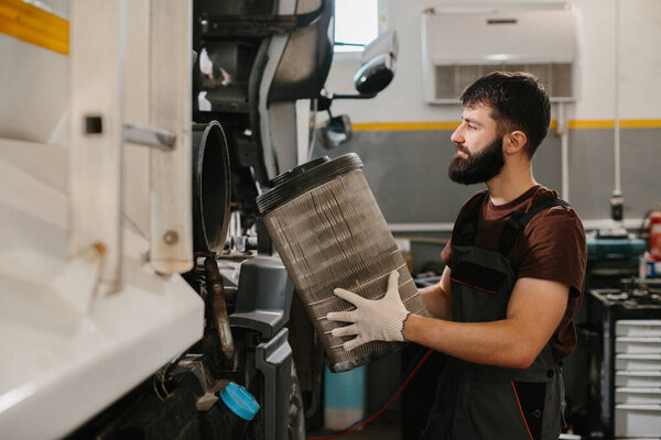 Auto mechanic expertly handles a large truck air filter in a professional garage setting, showcasing maintenance and repair skills