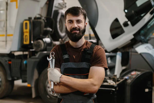 Anahtarları tutan kendinden emin bir tamircinin portresi, bir kamyon tamirhanesinde gülümseyen, otomotiv endüstrisinde uzmanlık ve profesyonellik sergileyen