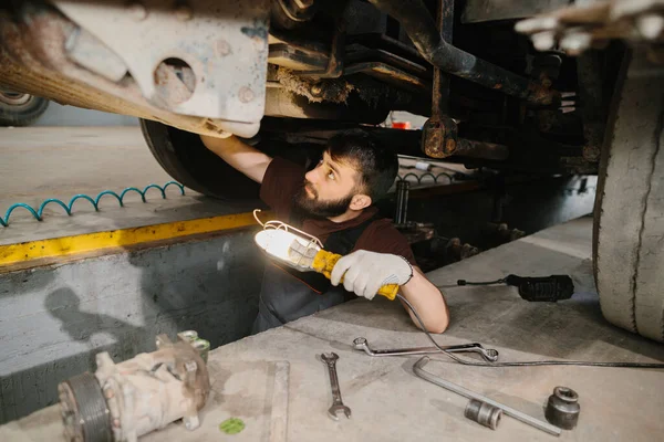 Tamircide bir kamyonun şasisini incelerken iş lambası kullanan oto tamircisi.