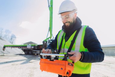 Gülen inşaat işçisi beton üretim tesisinde beton pompa uzaktan kumandası kullanıyor.