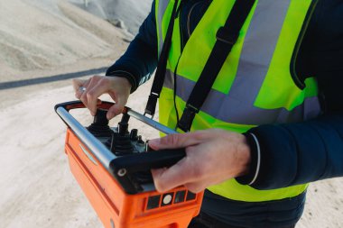 Çelik yelek giyen inşaat işçisi, beton üretim tesisinde uzaktan kumandayı kullanarak hassas ve verimli operasyonlar sağlıyor.