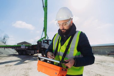 Çelik yelek giyen inşaat işçisi beton üretim tesisinde beton pompalı kamyon uzaktan kumandası kullanıyor.