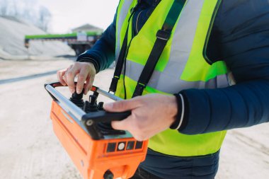 Çelik yelek giyen inşaat işçisi, beton üretim tesisinde uzaktan kumanda kullanarak, kesin kontrol ve verimli iş akışı sağlıyor.