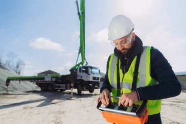 Beton üretim tesisinde uzaktan kumandalı beton bir pompa kamyonunu kontrol eden inşaat işçisi, hassasiyet ve uzmanlıkla makineleri yönetiyor.