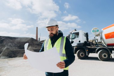 İnşaat mühendisi beton üretim tesisinde çimento karıştırıcı kamyonunun yanındaki planı inceliyor.