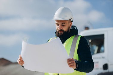 İnşaat mühendisi, inşaat sürecinde kalite ve verimliliği sağlamak amacıyla bir beton üretim fabrikasının planlarını inceliyor.