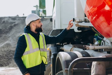 Üretim tesisinde çelik yelek ve kask giyen inşaat işçisi beton karıştırıcı kamyon kullanıyor.