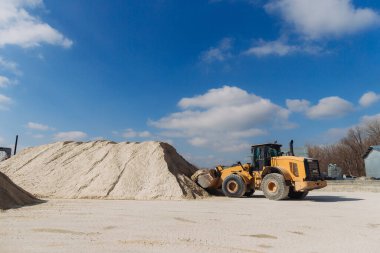 Parlak mavi gökyüzünün altındaki beton üretim tesisinde kumla çalışan güçlü bir tekerlek yükleyicisi.